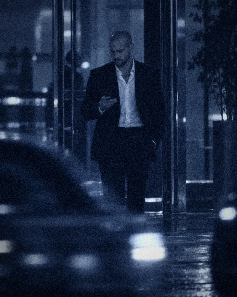 Surveillance-style photo of Flavien walking out of a building at night, reading his phone